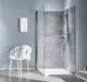 Weißer E-Komfortdurchlauferhitzer in einem modernen Badezimmer, montiert an einer Wand. Die Dusche ist in einem minimalistischen Stil gestaltet, mit grauen Fliesen. CLAGE Logo sichtbar.